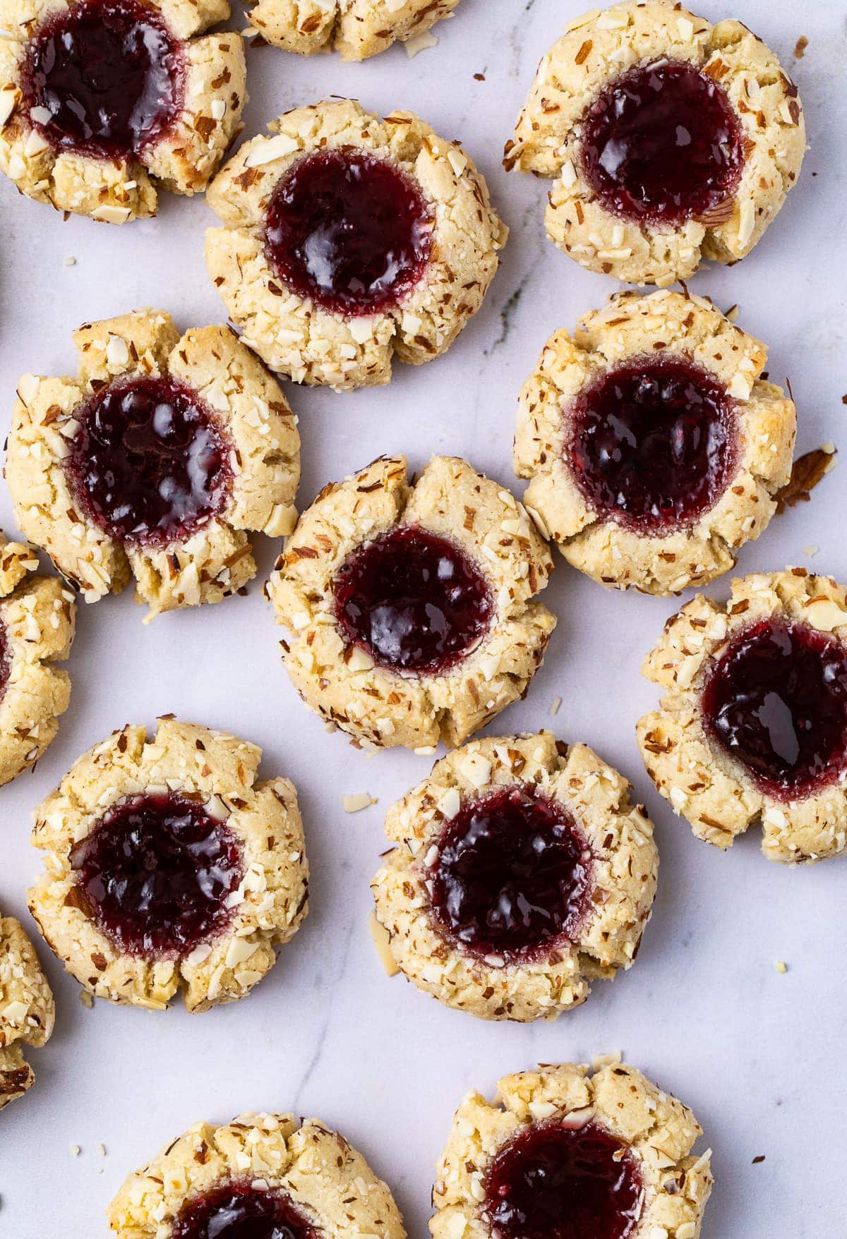 top down view of freshly made almond flour thumbprint cookies on a marble slab.