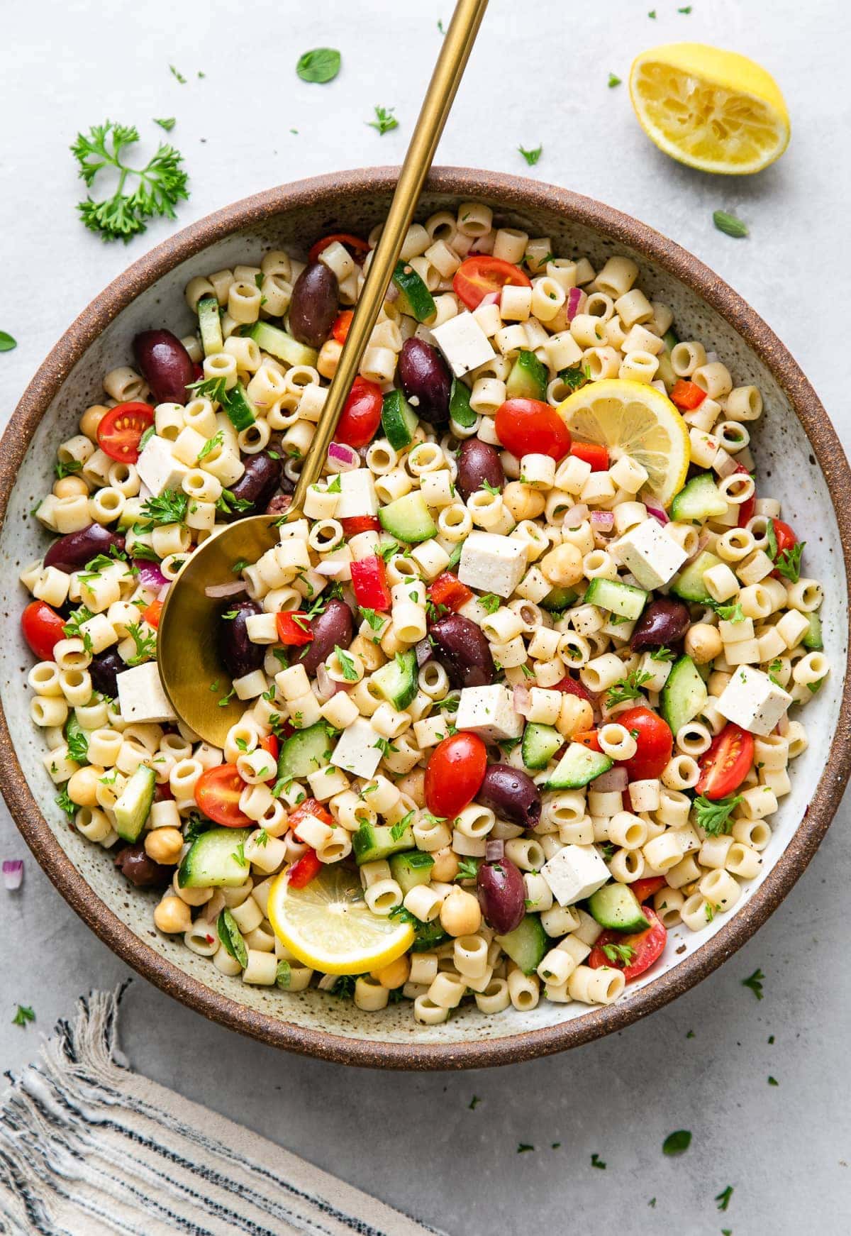 top down view of healthy, vegan Greek pasta salad in a serving bowl with gold serving spoon.