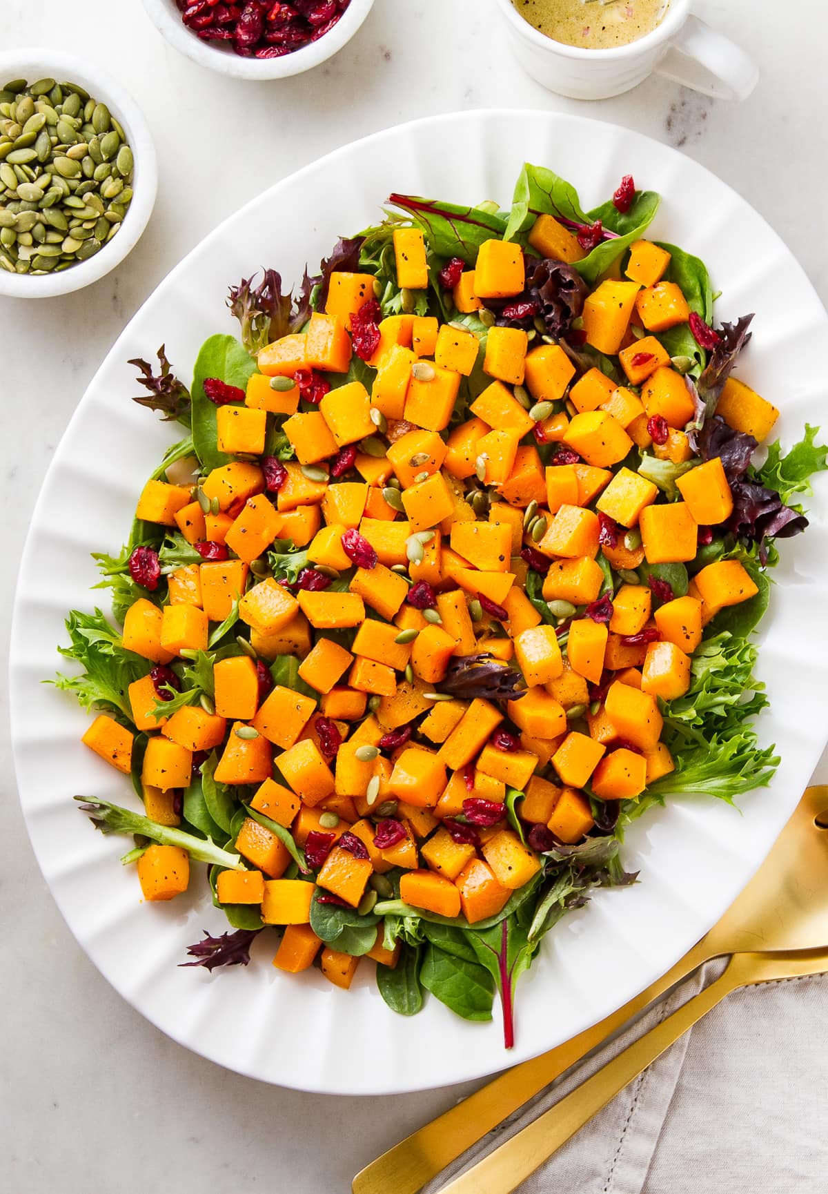 top down view of butternut squash salad with cranberries and shallot vinaigrette on a serving platter.