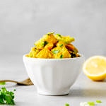 head on view of healthy curried potato salad in a small white bowl with items surrounding.