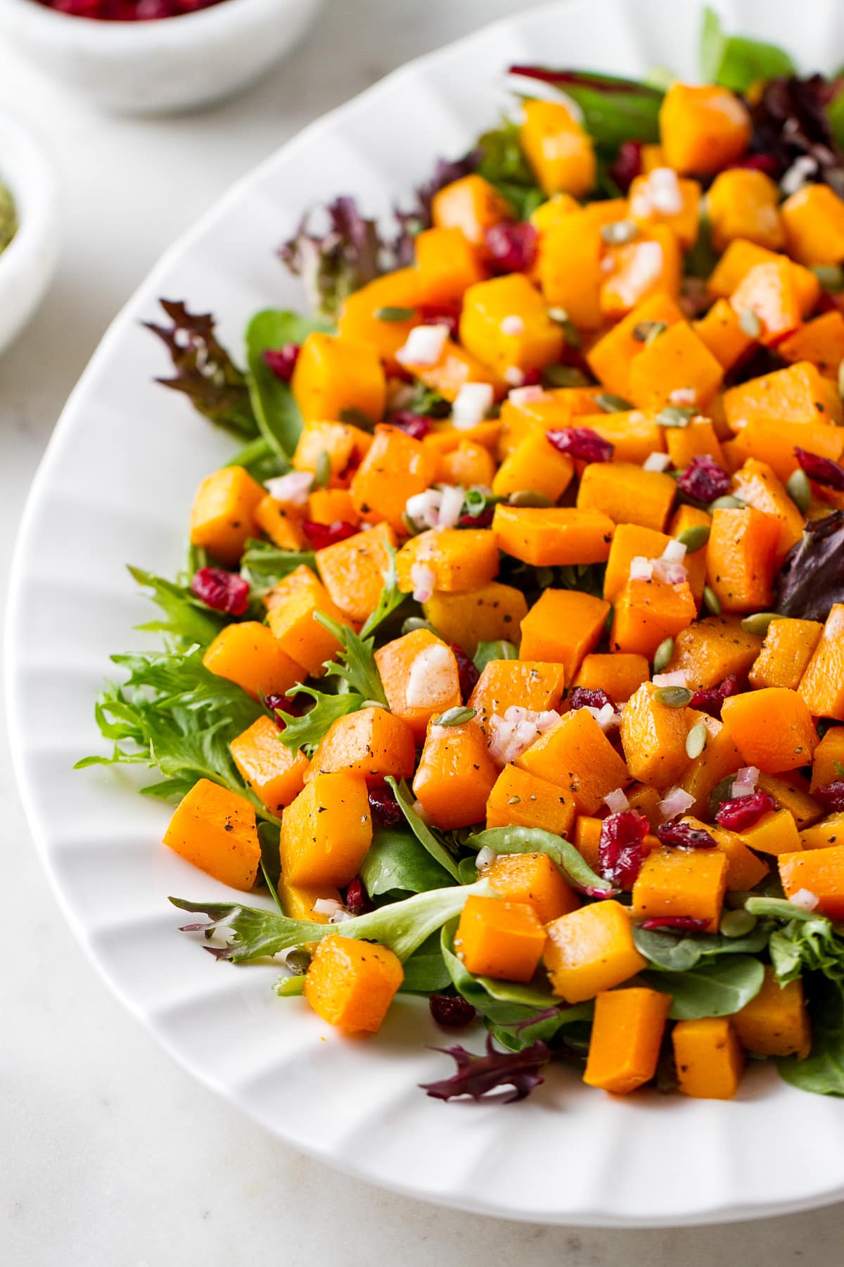 side angle view of butternut squash salad with cranberries and shallot vinaigrette on a serving platter.