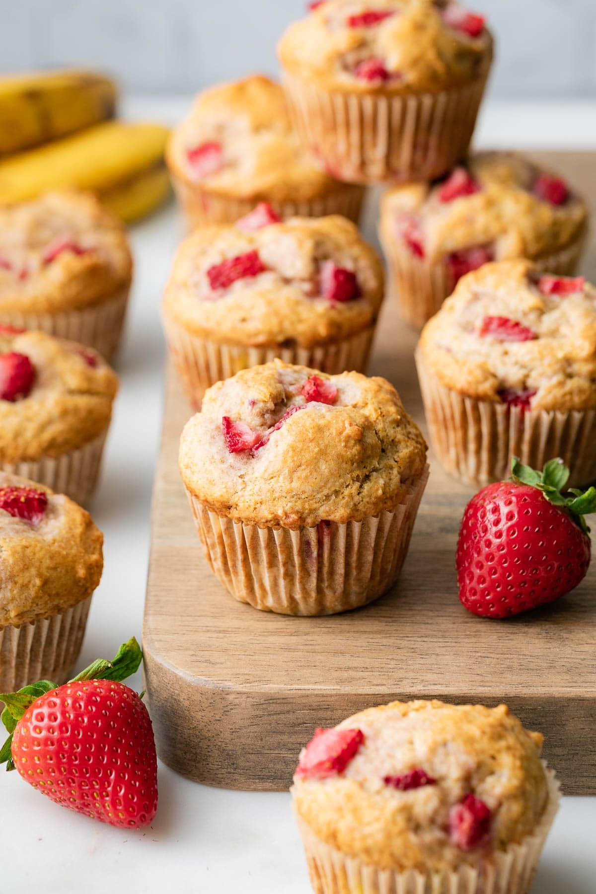 side angle view of batch of healthy strawberry banana muffins on wooden serving board.