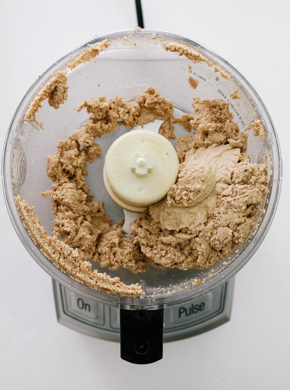 top down view of homemade almond butter in a food processor after being processed for about 10 minutes, clumpy in formation