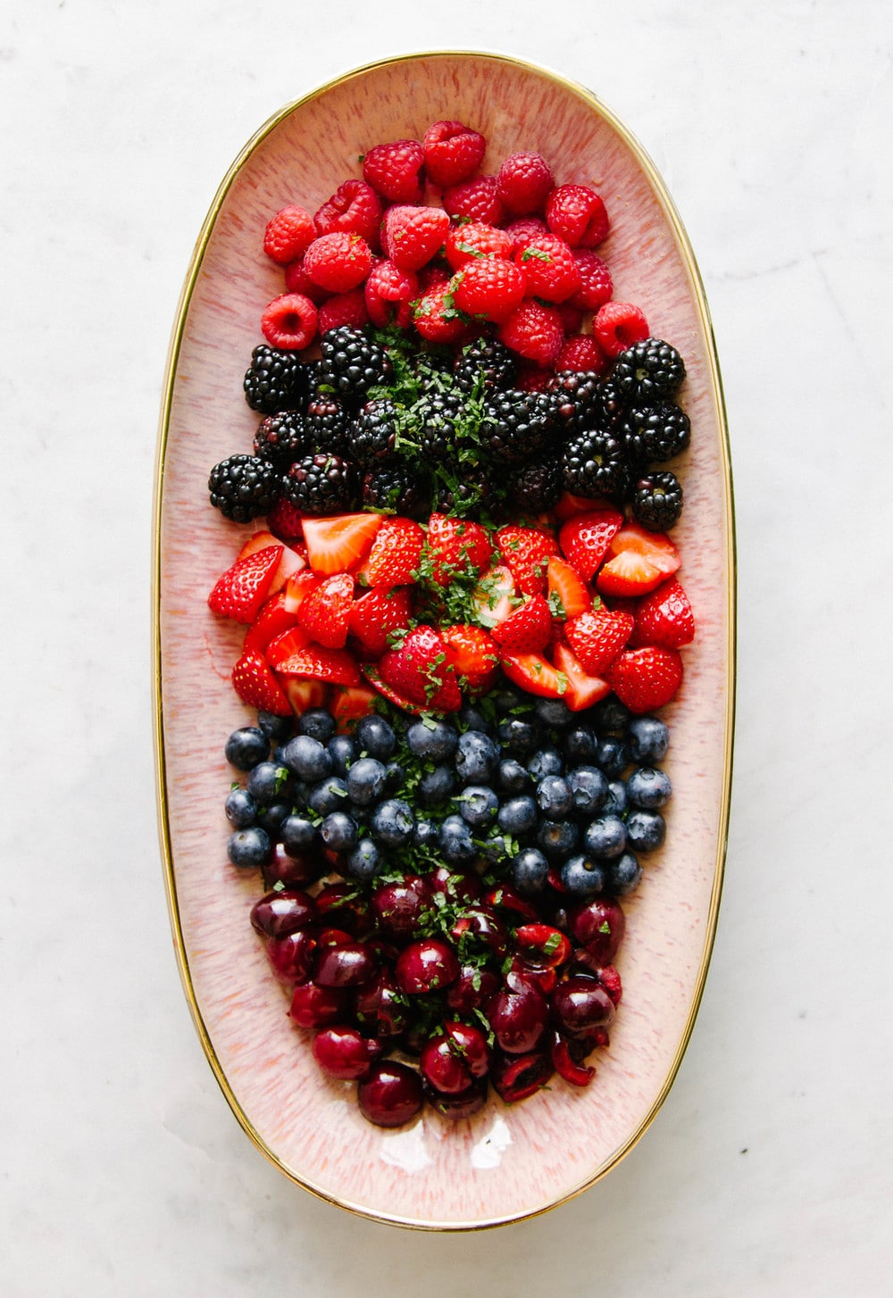cherries, blueberries, strawberries, blackberries and raspberries on a pink plater sprinkled with fresh mint